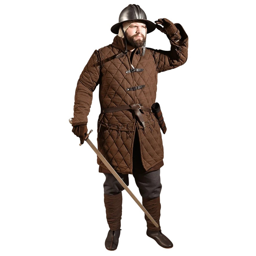 A man wearing a medieval-style brown quilted coat, helmet, gloves, and dark trousers, holding a sword against a plain white background.