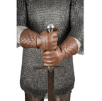 A person wearing medieval-style brown quilted leather gloves and a chainmail tunic, holding a sword with a silver pommel against a plain white background.