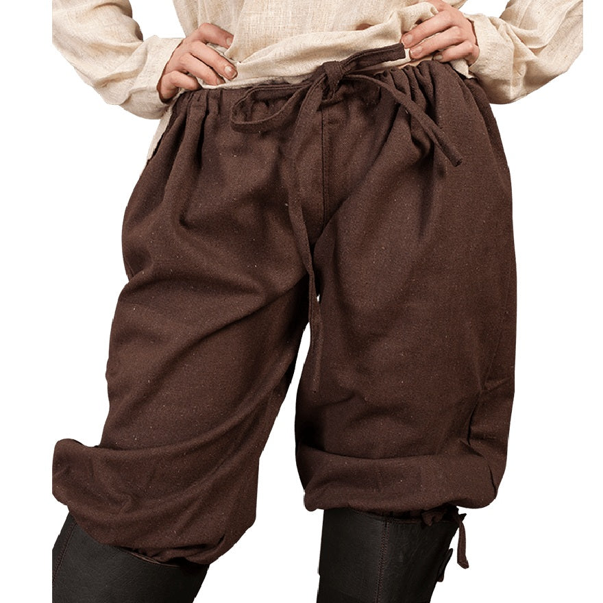 A person wearing loose brown drawstring pants with a gathered waist and cuffed hems, paired with a light beige top and black leggings, shown against a plain white background.