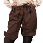 A person wearing loose brown drawstring pants with a gathered waist and cuffed hems, paired with a light beige top and black leggings, shown against a plain white background.