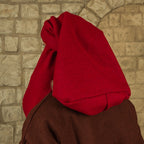 A person wearing a bright red hood or veil over a brown garment, photographed from the back against a light stone wall.